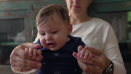 Baby sitting upright in mother’s hands, looking forward with curiosity, engaged and focused, early exploration, childhood discovery, bonding and nurturing moment © Marco