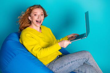Young woman with yellow sweater sits on blue bean bag smiles while using a laptop