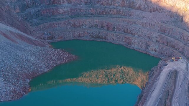 Reflective quarry lake filling deep terraced excavation with emerald water. Mirror like mining pit accumulating water among stepped rock walls. Flooded open pit quarry forming artificial reservoir
