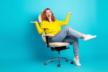Young woman in yellow sweater sits in an office chair smiling and gesturing against a bright blue...