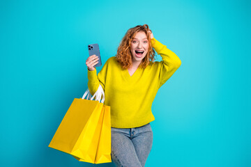 Happy young woman with yellow sweater shopping bags smiling against bright blue background