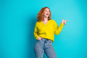 Beautiful young woman with yellow sweater smiling and pointing against a bright blue background