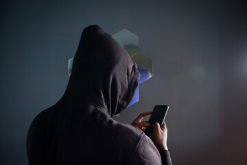 Anonymous man wearing black hoodie using smartphone indoors with his back to the camera, Phone Scammers, mysterious person typing message on mobile phone © eza