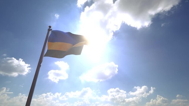 Rwanda Flag waving on a Flagpole from a Moving Angle in front of a blue sky with clouds	