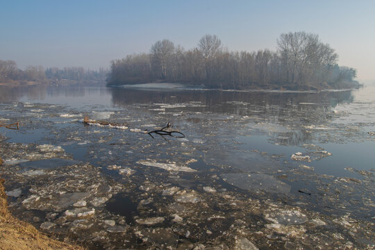 A river with ice floes, bare trees on the banks under a clear blue sky
