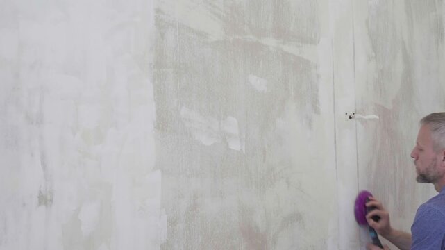 Man prepping surface with sanding vacuum, gentle final passes removing residue, readying plaster for primer and paint, concentrated careful motions