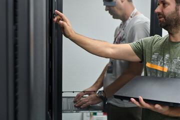 IT technicians working in a data center server rack with laptop performing maintenance and...