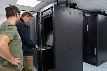 Data center technicians troubleshoot rack-mounted servers using a pull-out console laptop during...