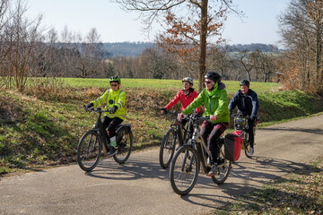 Obraz premium Group of active seniors enjoying a bicycle tour on a sunny spring day in the Swabian Forest, Germany. Friends cycling together through nature, promoting healthy lifestyle, recreation, and outdoor
