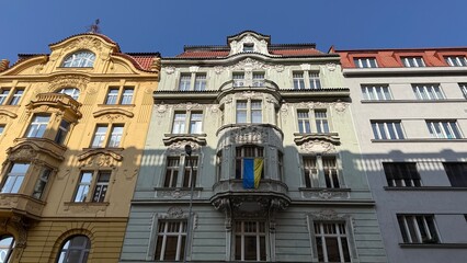 Obraz premium Old buildings stand side by side on a street in Prague with clear blue skies above during the day