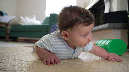 Fototapeta premium Baby lying on mat, curious expression, early development, tummy time, motor skills, exploring surroundings, infant growth, learning, childhood milestone, focused gaze