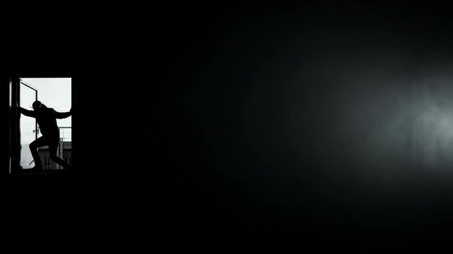 Silhouette of a man climbing through a window at night. Thief breaking into building. Crime concept, intruder sneaking into house secretly. Mystery and thriller.