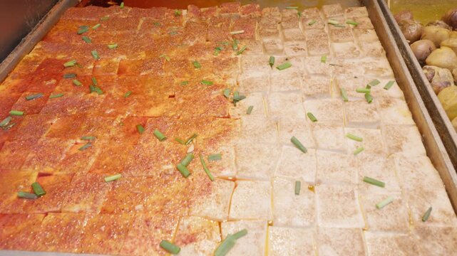 Traditional Asian street food preparation with seasoned tofu squares arranged with spices and garnished with green onions on a market tray, showcasing authentic street food preparation