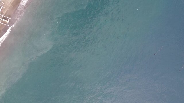 Cinematic top-down aerial drone tilt-up reveal from ocean surface to Amed Beach and Mount Agung volcano, Bali, Indonesia.