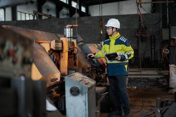 Factory worker operating machine tool and inspecting industrial equipment in workshop