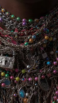 Vertical video: Camera shifting nudging chains on neck in dim light, revealing blue stone and locks