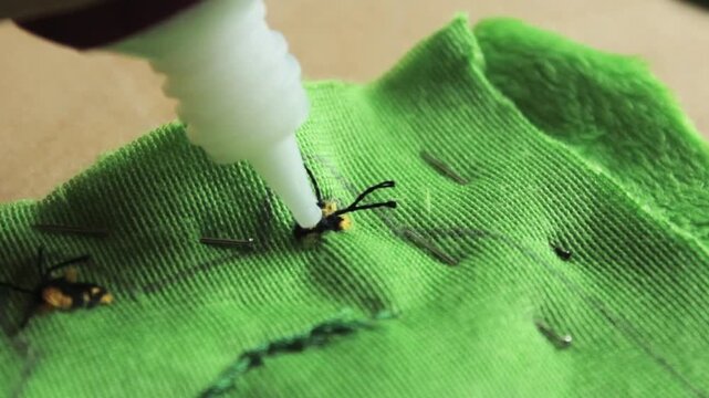 Applying Fabric Glue to Secure Threads Inside Green Fabric &mdash; Handmade Toy Crafting Process Close-Up