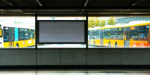 Fototapeta premium Dark tunnel reveals yellow buses behind glass panels. Concrete structure creates strong light contrast. Empty platform suggests transit station.