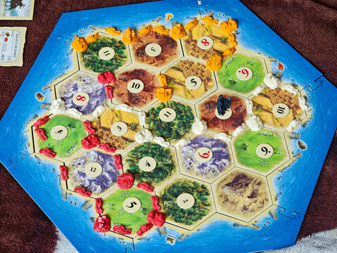 Catan board game in progress full board with colorful game pieces number tokens, strategic tabletop gameplay setup on hexagon island map, resource management planning concept, closeup detail no people
