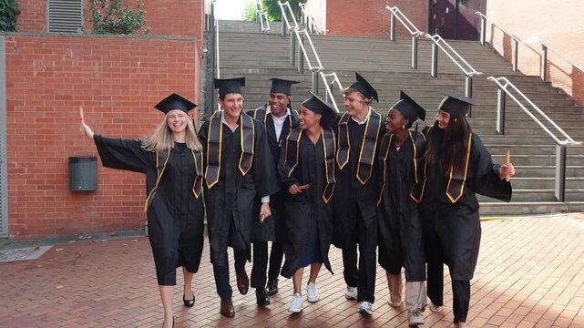 Group of diverse university students in cap and gown walking and celebrating together after their graduation ceremony at the campus