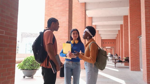 Group of three multicultural friends happily talking in a university hallway. Young diverse students socializing and enjoying a conversation