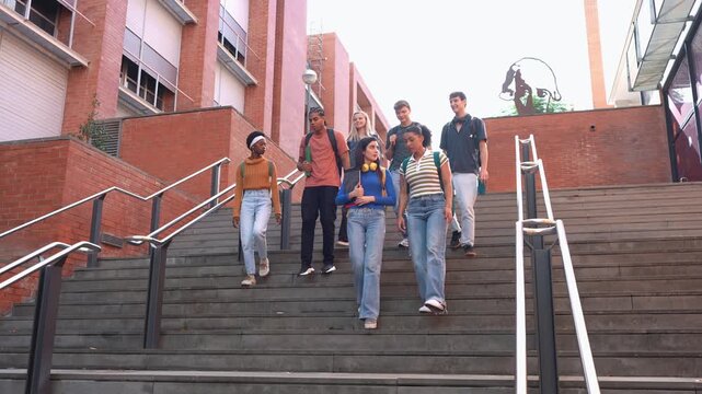 Multiethnic group of young university students walking down the stairs of the campus while happily talking after class in the college yard