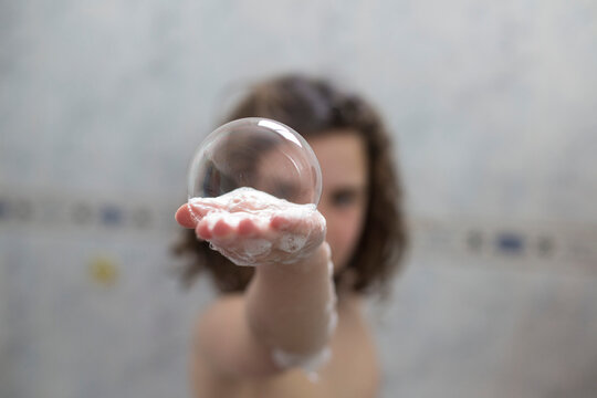 Girl standing in a shower  holding a large soap bubble in the palm of her hand