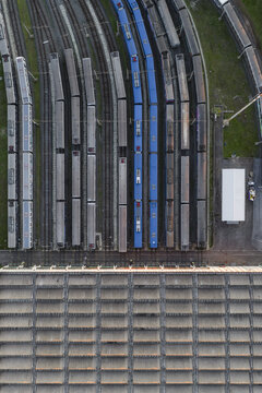 Aerial view of rows of trains, some a striking blue, sit parked on multiple parallel tracks next to a large building, Rome, Lazio, Italy.
