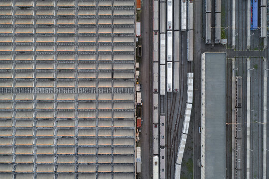 Aerial view of a vast industrial landscape unfolds, with rows of silver trains juxtaposed against the geometric grid of a massive warehouse, Rome, Lazio, Italy.