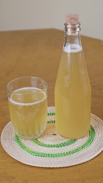 Green tea kombucha in clear glass bottle and drinking glass on wooden table vertical video. 