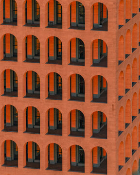Aerial view of a building facade featuring rows of arched windows casting deep shadows, its warm terracotta hues contrasting sharply with the cool interiors, Rome, Lazio, Italy.