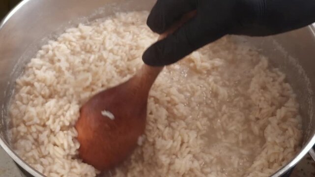 Close-up of unpolished brown rice being stirred with a wooden spoon while cooking in a pot