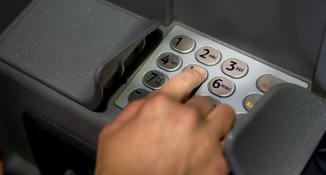 Hand at an ATM, entering the PIN, withdrawing money