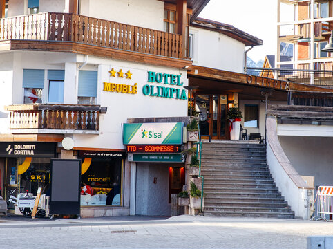 Cortina D Ampezzo, Italy - March 07, 2026: Hotel Olimpia building with three stars sign, stairs leading to entrance, and nearby shops in a winter sports destination