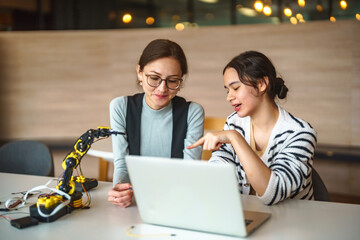 Two young women collaborating on a robotics project with a laptop and robotic arm © FotoArtist