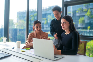 Diverse team collaborating on a laptop in a modern office with city views © FotoArtist