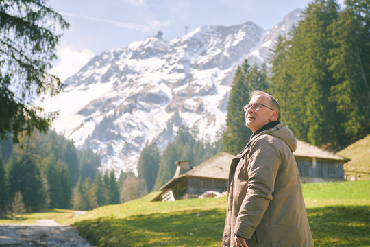 Middle age man hiking near Moleson mountain in Gruyere Switzerland with alpine chalet, forest and snowy peaks under clear sky scenic Swiss landscape
