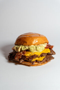Double smash cheeseburger with bacon and green avocado guacamole sauce on a brioche bun isolated