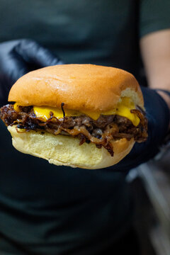 Chef in black gloves holding an authentic Oklahoma fried onion burger with thinly sliced onions and melted cheese