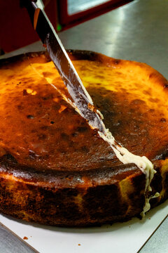 Chef using a knife to slice a creamy burnt basque cheesecake with a golden crust in a professional kitchen