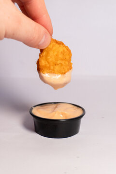 Hand dipping a crispy golden chicken nugget into a creamy pink thousand island dipping sauce isolated on white