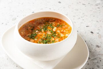 A white bowl of traditional Romanian meatball soup (ciorbă de perișoare) served on a plate,...