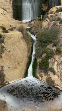 Stunning view of the elche reservoir dam, with water flowing over its edge creating a beautiful artificial waterfall in a rocky, arid canyon landscape in alicante, spain