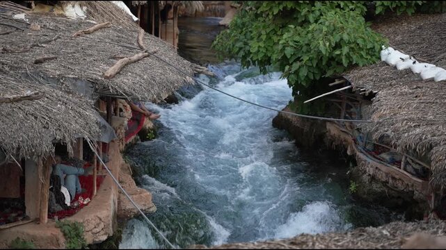 Scenic view of traditional rustic cafes with thatched roofs built over the fast-flowing Oum Er-Rbia river springs in the Middle Atlas mountains, Morocco.
