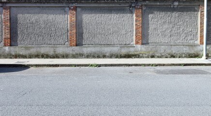 Naklejka premium Grunge rough concrete wall with rough brick columns. Tiled sidewalk and street in front. Urban background for copy space.