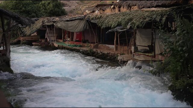 Scenic view of traditional rustic cafes with thatched roofs built over the fast-flowing Oum Er-Rbia river springs in the Middle Atlas mountains, Morocco.