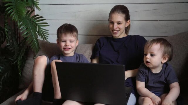 White sister and two boys watching laptop together on couch, animated faces reacting to content, little brother giggles, relaxed posture, indoor plant framing scene, gentle afternoon light, collective