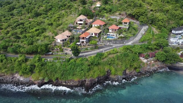 Cinematic aerial drone pulling out to reveal wide view of Amed coastline and surrounding hills in Bali, Indonesia.