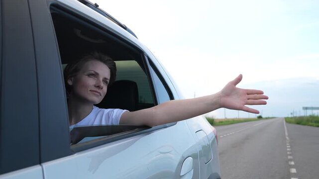 Lady leaning from car with arm outstretched, savoring open road, countryside adventure, carefree journey, genuine smile, blue sky ahead, exploring new destinations, pleasant weather, sense of optimism