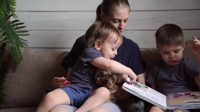 Toddler happily turns pages with older brother. Playful hands flip pages of colorful storybook on couch. Lively family moment with child discovering pictures alongside sibling in cozy home setting